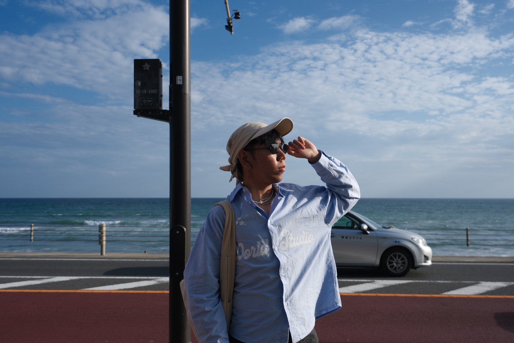 Adrian on the coast, hand raised to his sunglasses, the ocean behind him